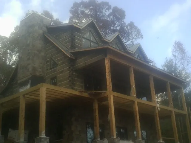 Stone chimney and dormers on a large log home with a timber porch in Kent